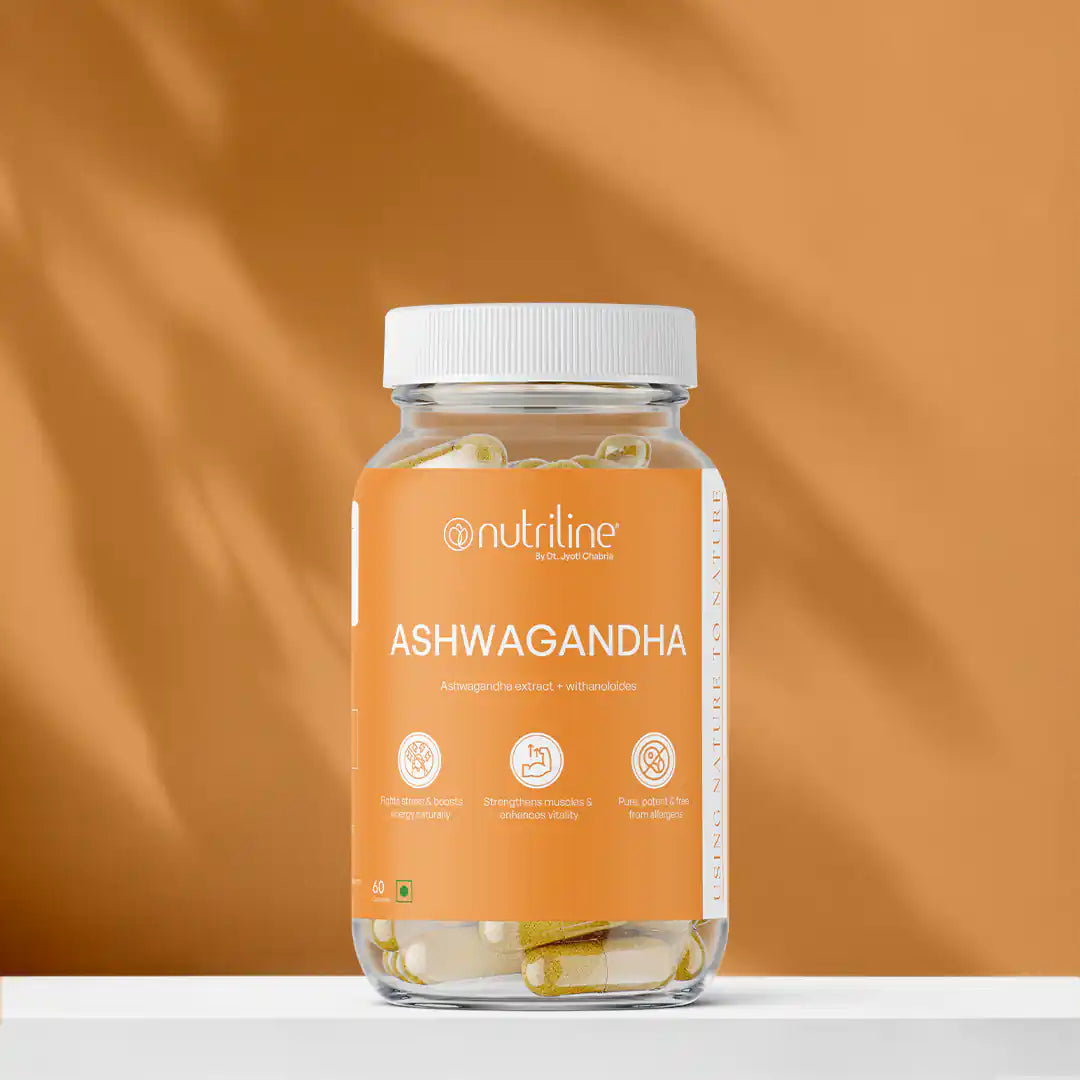 A clear jar labeled Ashwagandha filled with capsules rests on a white surface against a warm orange background. The label highlights benefits such as stress relief and muscle strength.