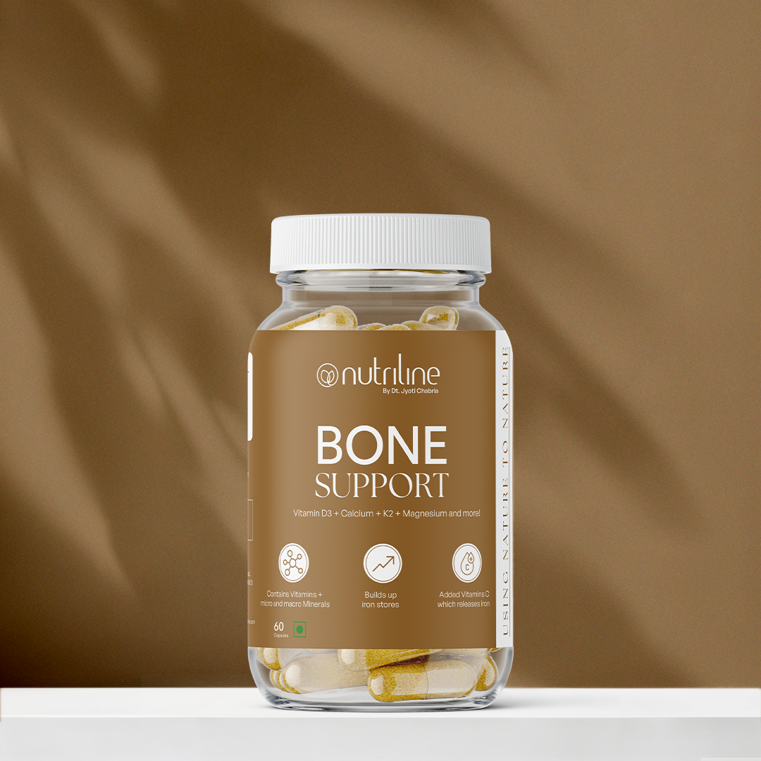 A clear bottle of Bone Support capsules with a white lid and beige label featuring Vitamin D3 info, placed on a white surface against a brown background.