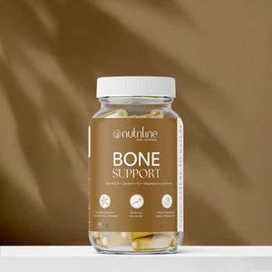 A clear bottle of Bone Support capsules with a white lid and beige label featuring Vitamin D3 info, placed on a white surface against a brown background.