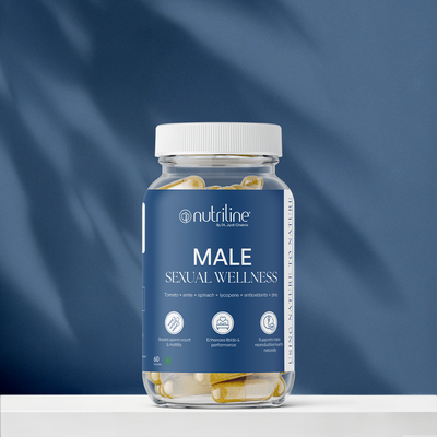 A clear bottle labeled Male Sexual Wellness sits on a white surface with a blue background, containing yellow and white capsules. The label lists tomato, amla, spinach, lycopene, and antioxidants to support testosterone boosting.